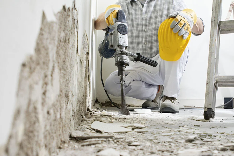 Worker using demolition hammer to remove damaged concrete from wall base in Garland, TX