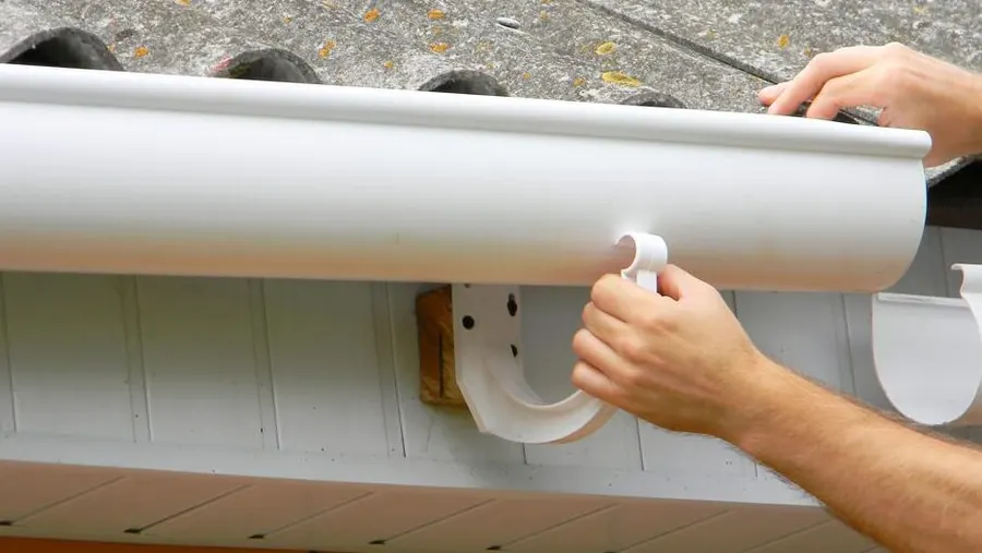 Contractor installing white PVC gutter system on residential home in Garland, TX