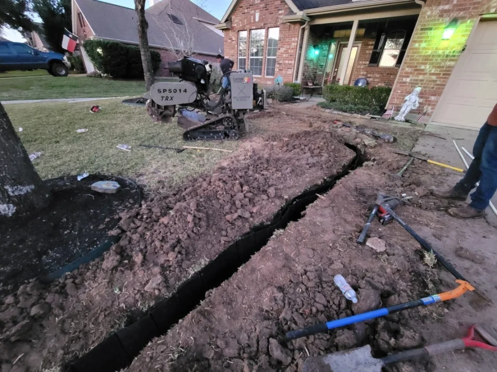 Root barrier installation in Garland, TX with trenching machine digging along home foundation