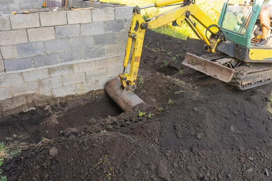 Mini excavator performing soil removal along foundation wall in Garland, TX